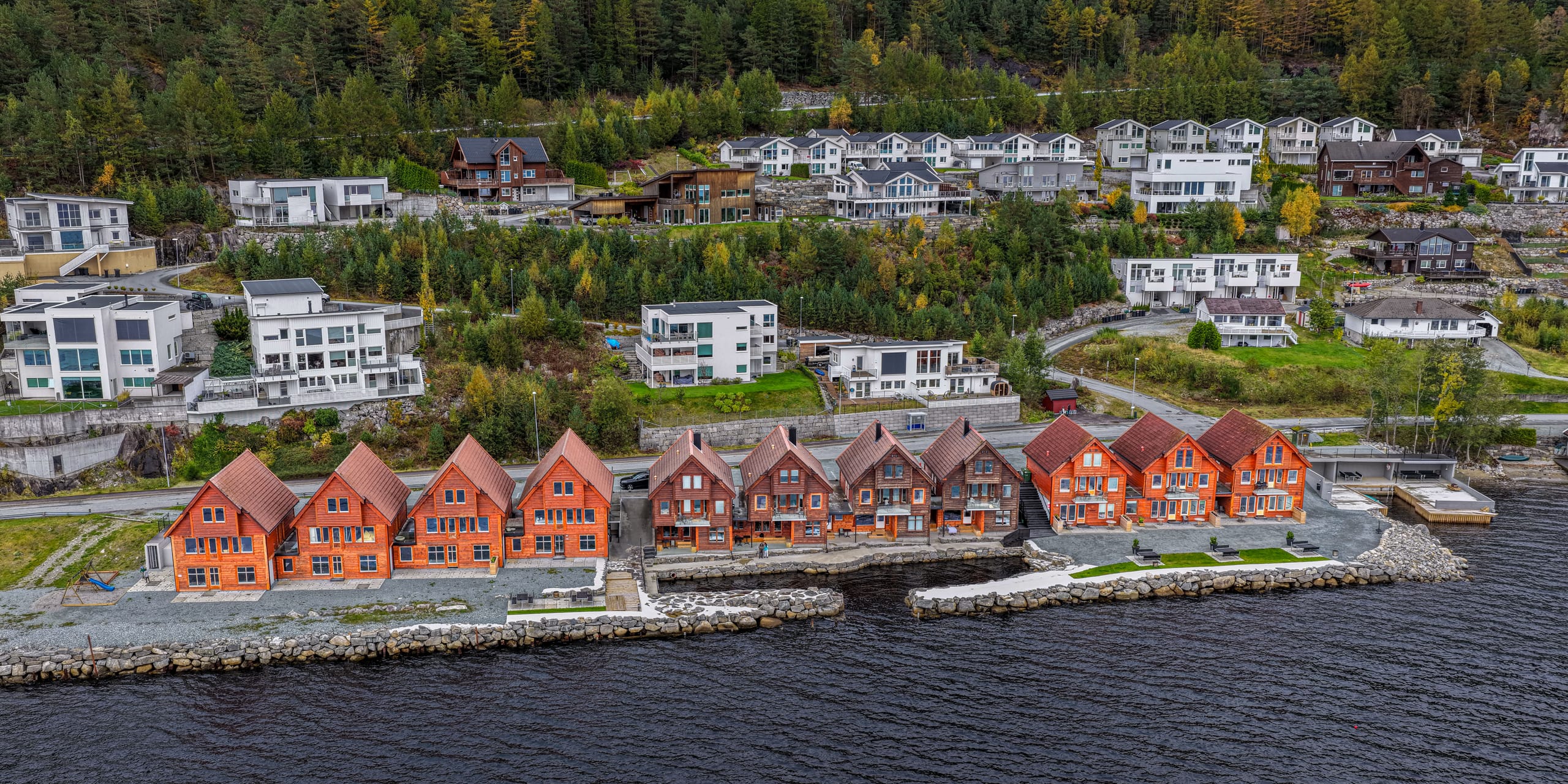 Preikestolen Panorama seen from the fjord, a row of cabins along the shoreline beneath forested hills